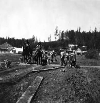 Working street in front of the school, where men are working on horses with dogs and children are crossing.