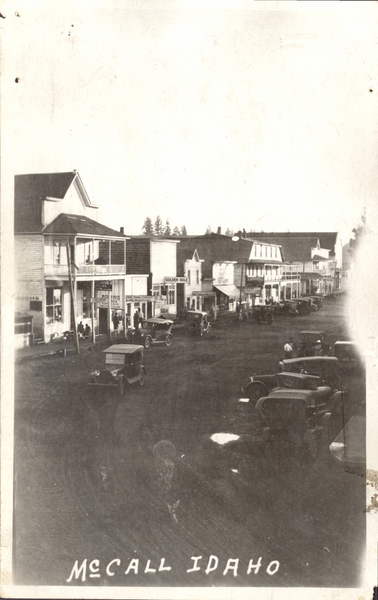 McCall, Idaho view of street with cars parked along the sides of the road, large building are in view like Golden rule, Drug store, ice cream parlor, and more. Image contains the text: "MCCALL IDAHO"