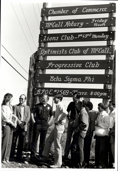 Sign dedication of businesses in McCall, the people are from left to right Sherri Curry, Judd Deboer, John Lyon, Bill Crowley, Dan Krahn, Unknown, Dalene Lembaes, Carol Standley, and Garry Standley. Image contains the text: "Chamber of Commerce McCall Rotary Lions Club Optimists Club of McCall Progressive Club Beta Sigma Phi B.P.O.E. 2569"