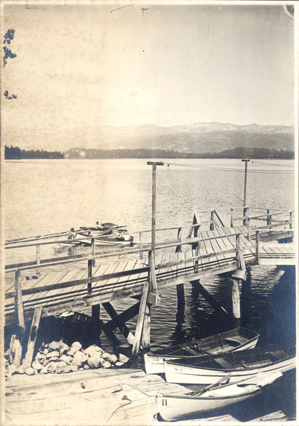 View of the mountains in the background, Payette lake, a public dock, with several boats on the water