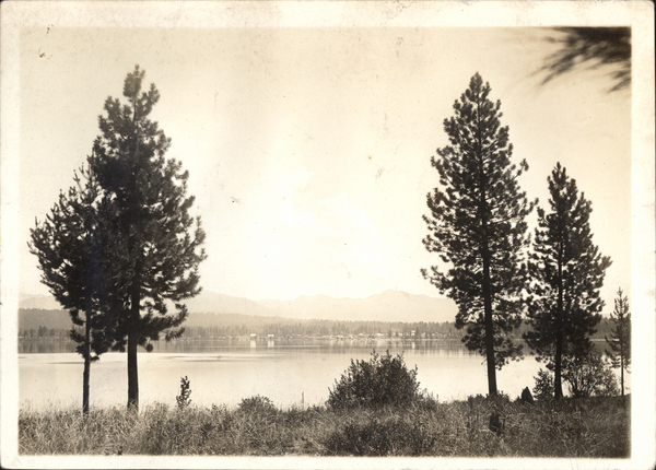 Large pine trees in the foreground, Payette Lake in the middle ground, and in the background McCall