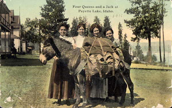 Four women on the front with a donkey with a pack, in the background there are pines, Payette lake, and old McCall buildings, On the reverse side it is a postcard to Mrs. JG Leitzke in Nampa, Idaho, the postage stamp was 1 cent, there are printed comments about migrations, the postcard also says, “ Dear Aunt, just a line to let you know we are at the lakes. There is plenty of work here. Will write more next time as I am working. - Chester Teater”. Image contains the text: "Four Queens and a Jack at Payette Lake Idaho"