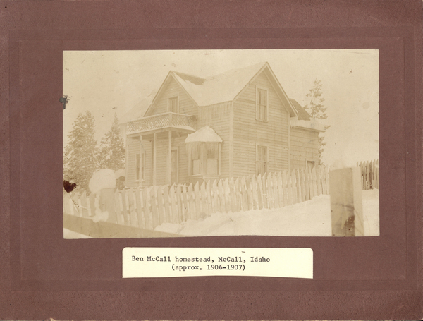 Ben McCall’s homestead in the winter, along with the house there is a snow covered fence and trees. Image contains the text: "Ben McCall homestead McCall Idaho approx 19061907"