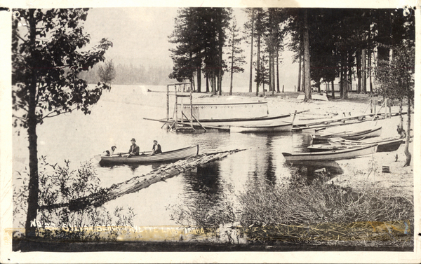 Original postcard with the view of Payette lake, along with some boats, and one boat with two people and a dog onboard in the lake. Image contains the text: "No 39 Miller Bros Payette Lake Idaho"