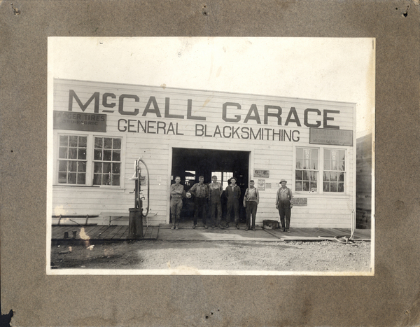 Front facing view of the McCall Garage, General Black Smithing, in front of the building there are six men standing for the photo. Image contains the text: "MCCALL GARAGE   GENERAL BLACKSMITHING   BADGER TIRES   MCCALL GARAGE"