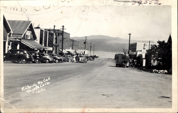 View of entering McCall with cars and buildings along the sides and in the background a mountain and Payette Lake. Image contains the text: "Entering McCall Payette Lakes Idaho  CAFE  Bayard"