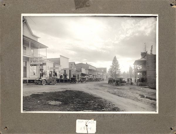 Photo on cardboard with a view of old McCall buildings like ice cream parlor, drug store, groceries along with additional buildings and cars on both sides, Property of Dan De Francesco