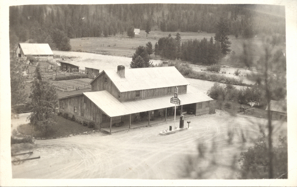 Original postcard of a large building and gas station on river: Cougar Mt. Lodge?. Image contains the text: "GAS   CABINS DRINKS"