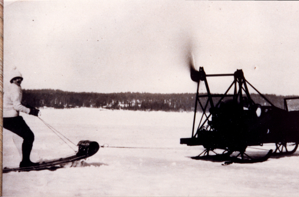 Frozen Payette Lake, in view there is women on a sled attached to an early snowmobile