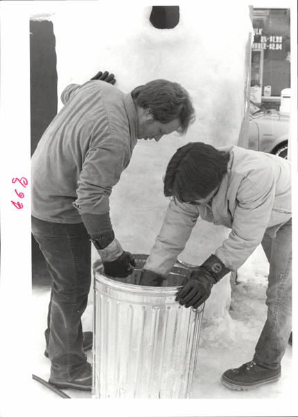 A man and women working on a ice sculpture together by preparing snow mix in a trash can. Image contains the text: "89"