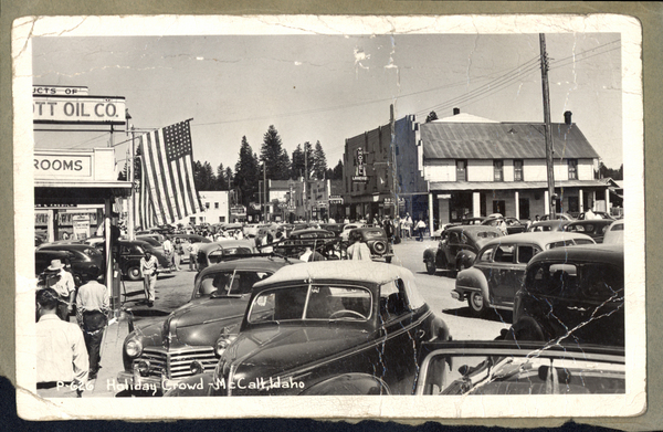 Original postcard on a piece of construction paper, P-626 Holiday Crowd- McCall, Idaho, in view lots of cars and people filling the street. Image contains the text: "Holiday Crowd McCall Idaho"