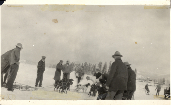 Dog sled and several men gathered around the dogs