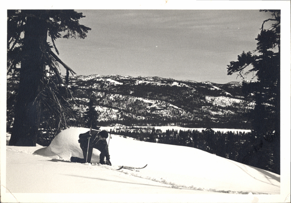 Lone skier adjusting skies, on reverse side “Typical cross-country terrain near McCall, Idaho. Frozen Payette Lake in background.”