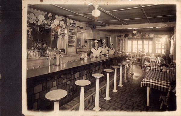 Inside view of a diner with three women behind the counter. Image contains the text: "Coca-Cola"