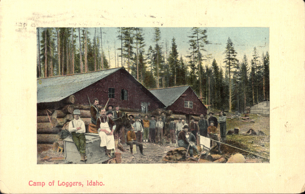 Original postcard of a crowd of men in front of red cabins. On the back there is a one cent postage stamp and states, “We are going to try to come out Saturday night phone if you can’t meet us or if you can come up town. Leonard. Mr. R. L. Smith Nampa, Idaho. R. D. no.2. Po box. 94. Mickey Fortin.”. Image contains the text: "Camp of Loggers Idaho"