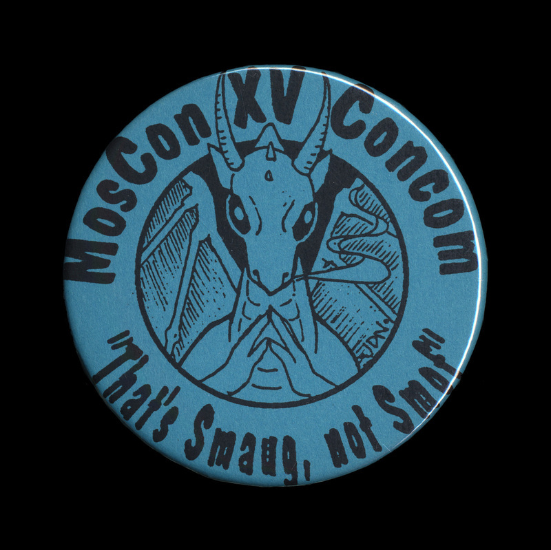 A blue, circular button with black text stating "MosCon XV Concom" at the top and the quote "'That's Smaug, not Smof"' at the bottom. In the middle of the button is an illustration of a cartoonified Smaug from J.R.R. Tolkien's The Hobbit. 