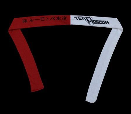 A red and white cloth headband that reads "Team MosCon" in English and "Cold Water Patrol" in Japanese. From the MosCon VII (1985) booklet, p. 15: "Overflowing as we are with new and innovative ideas, we actually accomplished one this year. Instead of the standard t-shirt or towel, we have, in limited supply, Team MosCon headbands. We chose headbands in part to provide our membership with a handy place to attach their nametags while in the jacuzzi, and also as a method of identifying the Con-com. (Ours are blue.) The idea was inspired by the film, Buckaroo Banzai. The Team MosCon logo was designed by Jacqualynn Duram and the Japanese was calligraphed by Ellen Thisted. The Japanese is pronounced, "Tsumetai mizu patororu-tai" and means "Cold Water Patrol." Get one quick. There will be a limited number of them for sale at the registration table."