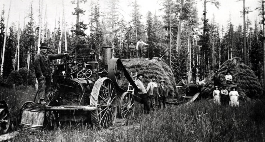 Stationary threshing outfit owned by Stiner Hellerud and threshing on his property west of the four corners at Park, Idaho. Early 1900s. Left to right: 1- Sigward Sunby (engineer), 2- Adolphe Swenson, 3- Chris Dahl, 4- Edwin Hellerud, 5- Lars Kaaen, 6- Stiner Hellerud, 7- Chris Jelleberg, 8 - Andrew Sunby, 9- Sylvester Flattery. Front row,[left to right:] 10- Josie Hellerud, 11- Axel Bohn, 12- woman in white on stack?, 13- Richard Hellerud, 14- Roy Bohn.