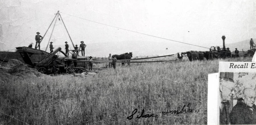 Steam engine-powered thresher on the Silas Imbler farm just northeast of Moscow in the 1890s. Looks like two teams of oxen in front of steam engine. The picture of the two men in right corner was due to being overlapped when picture of thresher copied. No identification of men.