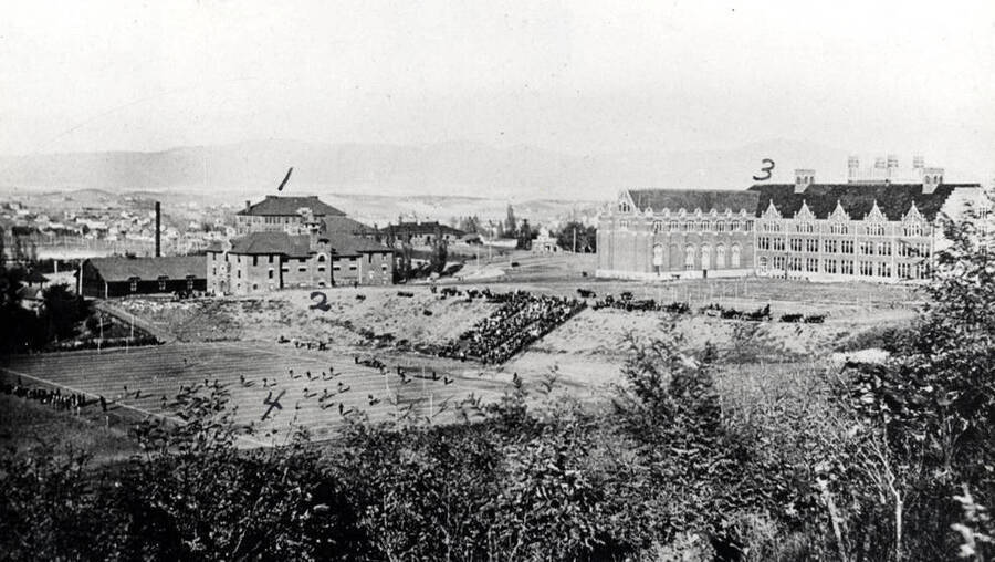 Looking northeast at University of Idaho buildings and athletic field. 1- Morrill Hall, 2- gymnasium, 3- Administration Building, 4- athletic field with football game in progress. About 1920.