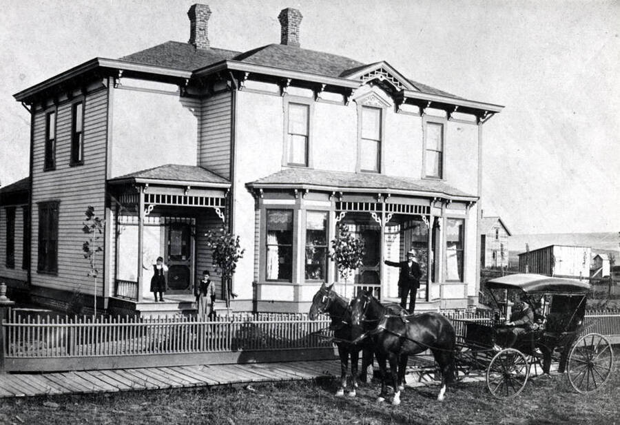 John Paulson residence built in the late 1880s or early 1900s at the southeast corner of Eighth and Washington streets. Left to right: R. Mabel, Mrs. Paulson, Mr. John Paulson, and Elmer in buggy. Picture 1893. Later, Elmer was a Latah County commissioner for many years.