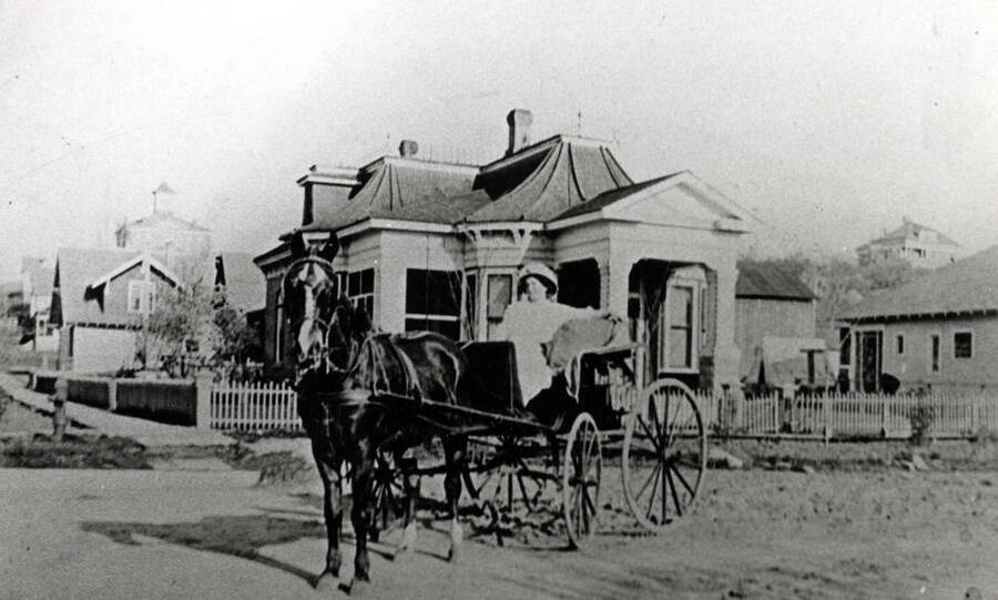 Mrs. Tom Tierney in buggy in front of their home at the southeast corner of Fifth and Washington streets about 1903. Huntback home beyond with the first Latah County Courthouse beyond. M.E. Lewis residence top right.