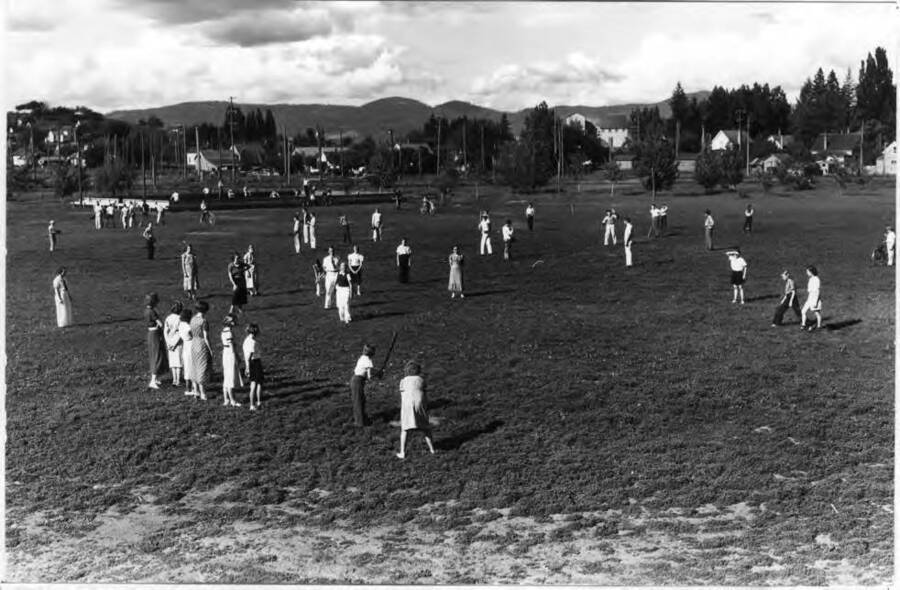 Looking northeast across the old Fair Grounds about 1938 at school children playing soft ball. Horseshoe courts beyond. Large white building is the Washburn-Wilson Seed Company warehouse, which burned July 7, 1945.