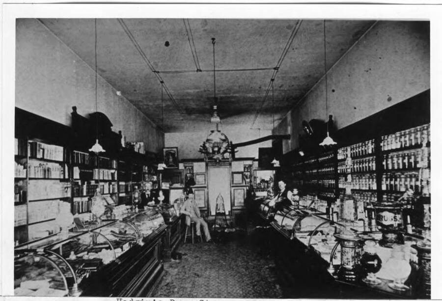 Located at the northeast corner of First and Main streets in the brick building replacing the original small wooden building. Roland Hodgins is the man behind the counter at the left. See picture number 21 book #2 for brick building.