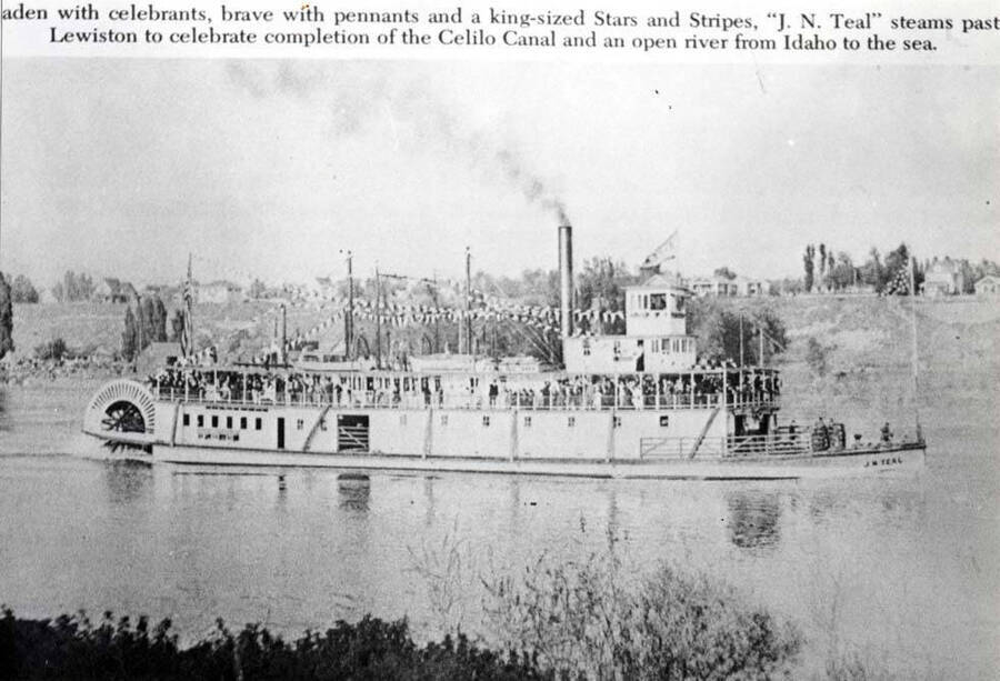 Laden with celebrants, brave with pennants and a king-sized Stars and Stripes, "J.N. Neal" steams past Lewiston to celebrate completion of the Celilo Canal and an open river from Idaho to the sea.
