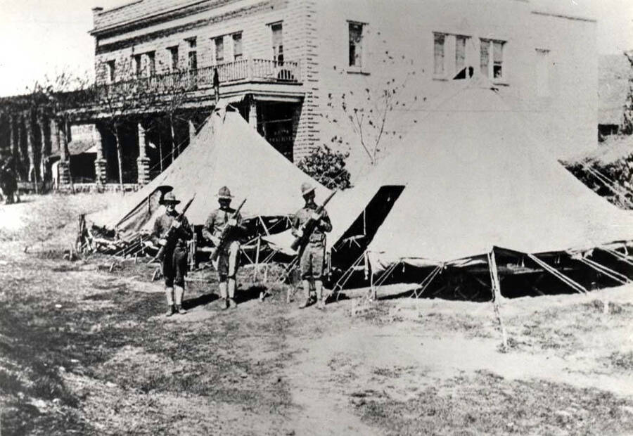 Hotel at Riparia, Washington with two squad tents in foreground. Privates Hubble, Starnes and Johnson standing at port arms in front of their tent. Picture taken in April 1917 before trees were completely leafed out. Clyde Dobkins, manager: hotel, store, post office.