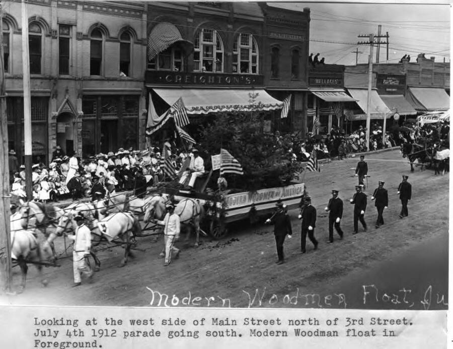 Looking at the west side of Main Street north of 3rd Street, modern Woodman float in foreground. July 4, 1912, parade going south. Modern Woodman float in foreground.