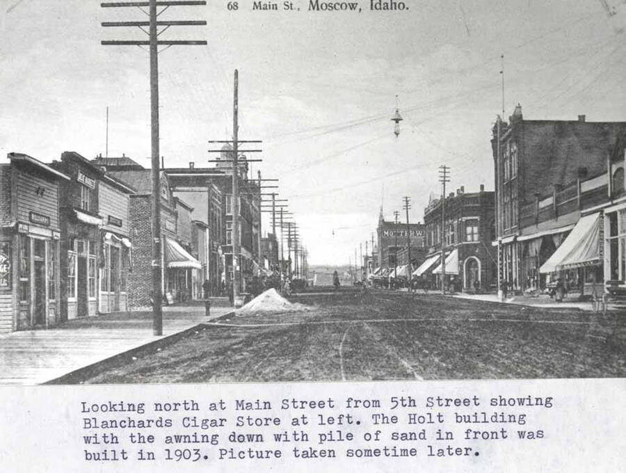 From Fifth Street showing Blanchard's Cigar Store at left. The Holt building with the awning down with pile of sand in front was built in 1903. Picture taken sometime later.