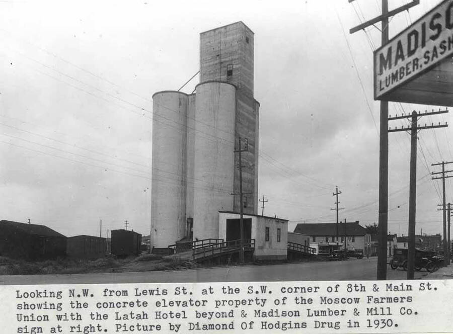 Showing the concrete elevator property of the Moscow Farmers Union with the Latah Hotel beyond and Madison Lumber and Mill Company sign at right. Picture by Dimond of Hodgins Drug in 1930.