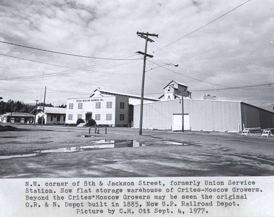 Formerly Union service station. Now flat storage warehouse of Crites-Moscow Growers. Beyond the Crites-Moscow Growers may be seen the original O.R. & N.  [Oregon Railroad and Navigation] depot built in 1885. Now U.P. [Union Pacific] Railroad depot. Picture by Clifford M. Ott September 4, 1977.