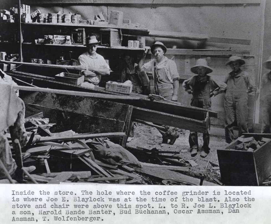 Inside the store. The hole where the coffee grinder is located is where Joe E. Blaylock was at the time of the blast. Also the stove and chair were above this spot. Left to right: Joe L. Blaylock, a son; Harold Bande Banter; Bud Buchanan; Oscar Assman; Dan Assman; T. Wolfenberger.