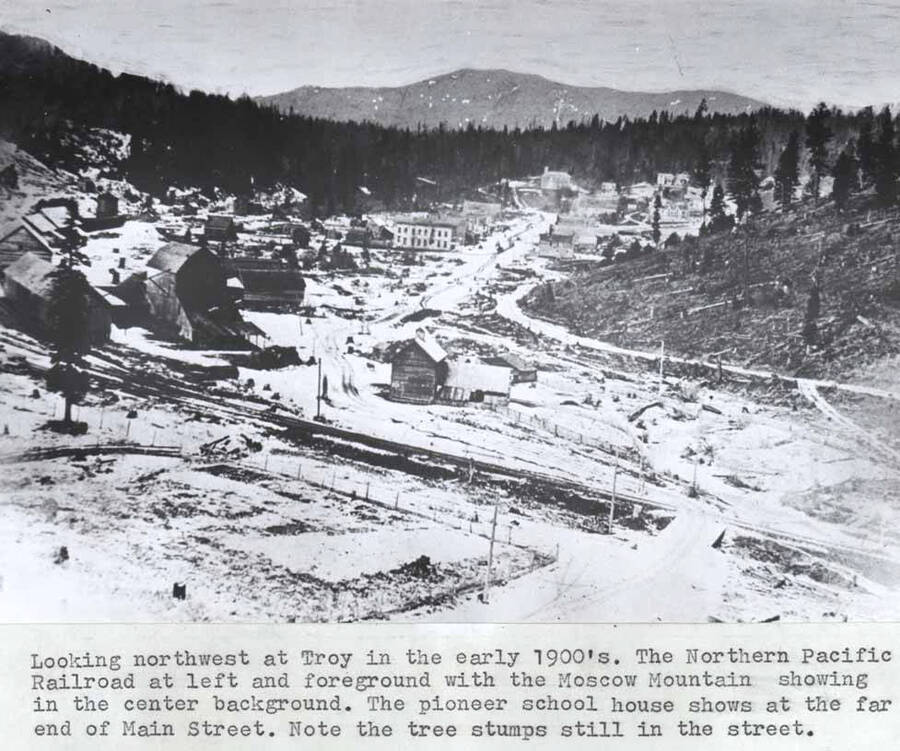 In the early 1900s. The Northern Pacific Railroad at left and foreground with the Moscow Mountain showing in the center background. The pioneer school house shows at the far end of Main Street. Note the tree stumps still in the street.