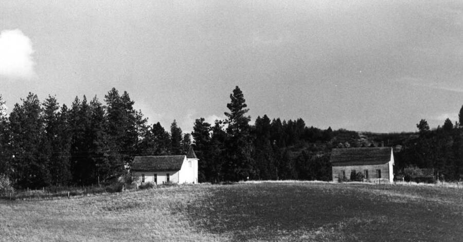 The church at left was built in 1907 and dedicated February 1908. The school at the right was built in the summer of 1903 and used until the fall of 1952 when students were taken by bus to Kendrick and Juliaetta. The above picture [90-5-103] was taken in 1973 by Clifford M. Ott. For three months, the first Gold Hill school in 1888-89 was f held in a log cabin known as the Bill Benner homestead; seven children [attended]. In the fall of 1890 a log school house was built on the top hill just south of the present school shown above [90-5-103]. The log school house was used for 12 years.