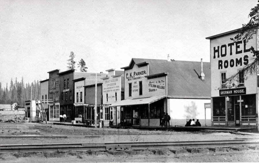 Looking east at the south side of Main Street between Railroad and First avenues. An early picture of Bovill before the post office was built where the three men are sitting on the sidewalk. A steam engine generating electric light plant was installed in 1911 and owned by the town.