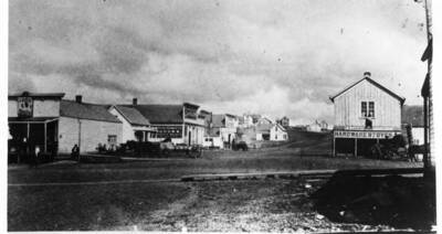 George [Gottfried] Weber Harness Shop on northeast corner; Langdon Hardware & Stage office on southeast corner.
