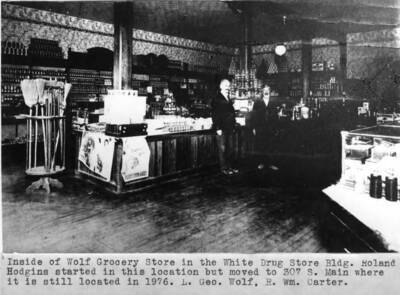 Roland Hodgins started in this location but moved to 307 South Main Street where [store] is still located in 1976. Left: George Wolf; right, William Carter.