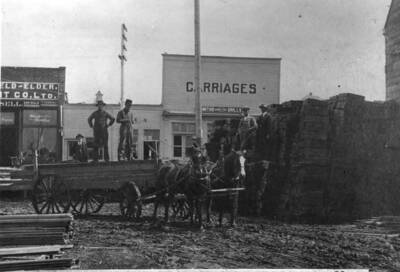 Man standing in back of wagon, Thore B. Thoreson father of H.B. (Curley) Thoreson, Chief of Police for many years; retired 1968. Building at corner of Main and Sixth streets. Top of courthouse above Thoreson's head.