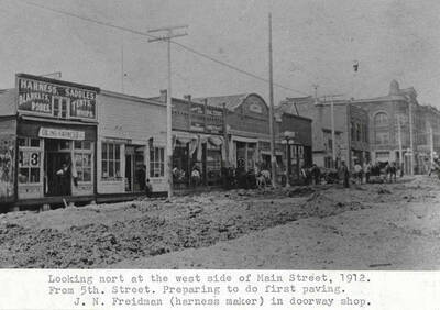 From Fifth Street. Preparing to do first paving. J.N. Freidman (harness maker) in doorway shop.