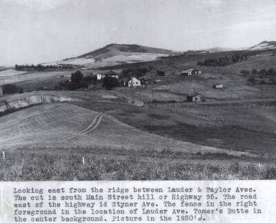 The cut is south Main Street hill or Highway 95. The road east of the highway is Styner Avenue. The fence in the right foreground is the location of Lauder Avenue. Tomers Butte in the center background. Picture in the 1930s.