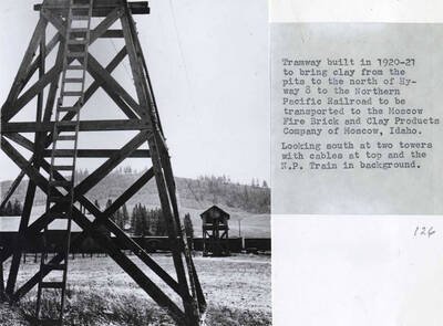 Built in 1920-21 to bring clay from the pits to the north of Highway 8 to the Northern Pacific Railroad to be transported to the Moscow Fire Brick and Clay Products Company of Moscow, Idaho. Looking south at two towers with cables at top and the Northern Pacific Railroad train in background.