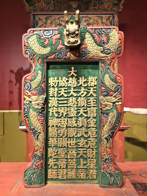 Carved and brightly painted wooden altar tablet or spirit tablet framed with golden dragons and dragon head, with gilded chinese characters honoring multiple deities, used for worship at traditional chinese temples.