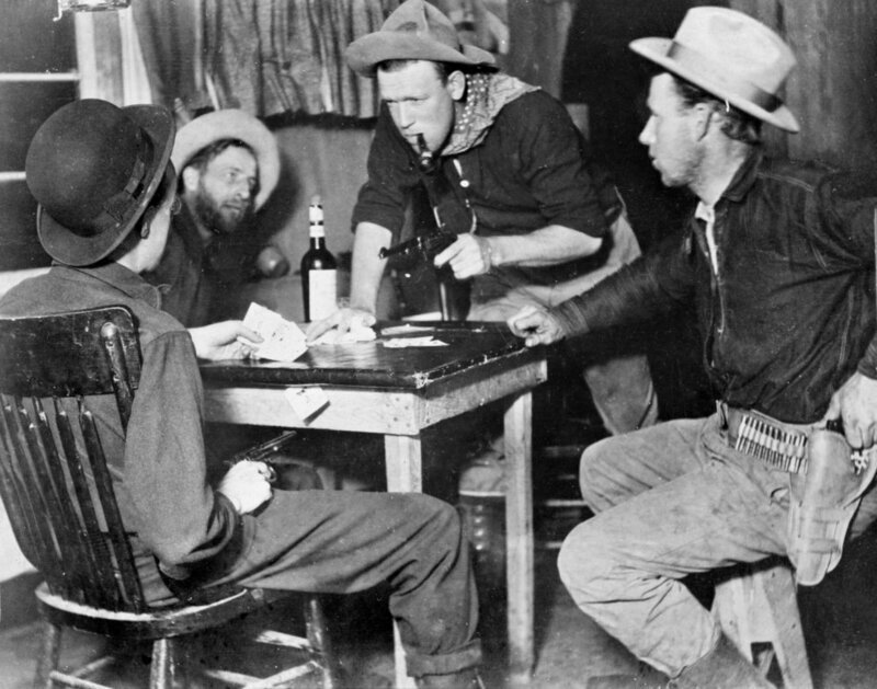 Men holding guns during a game of cards.