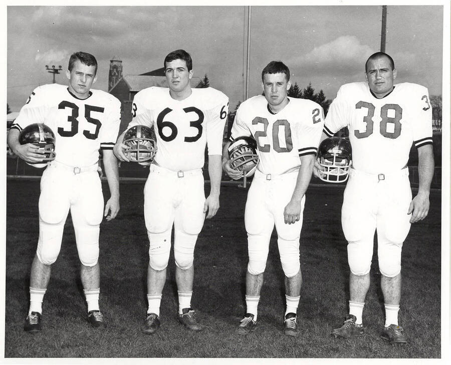Four University of Idaho football players holding their helmets and wearing full football gear.