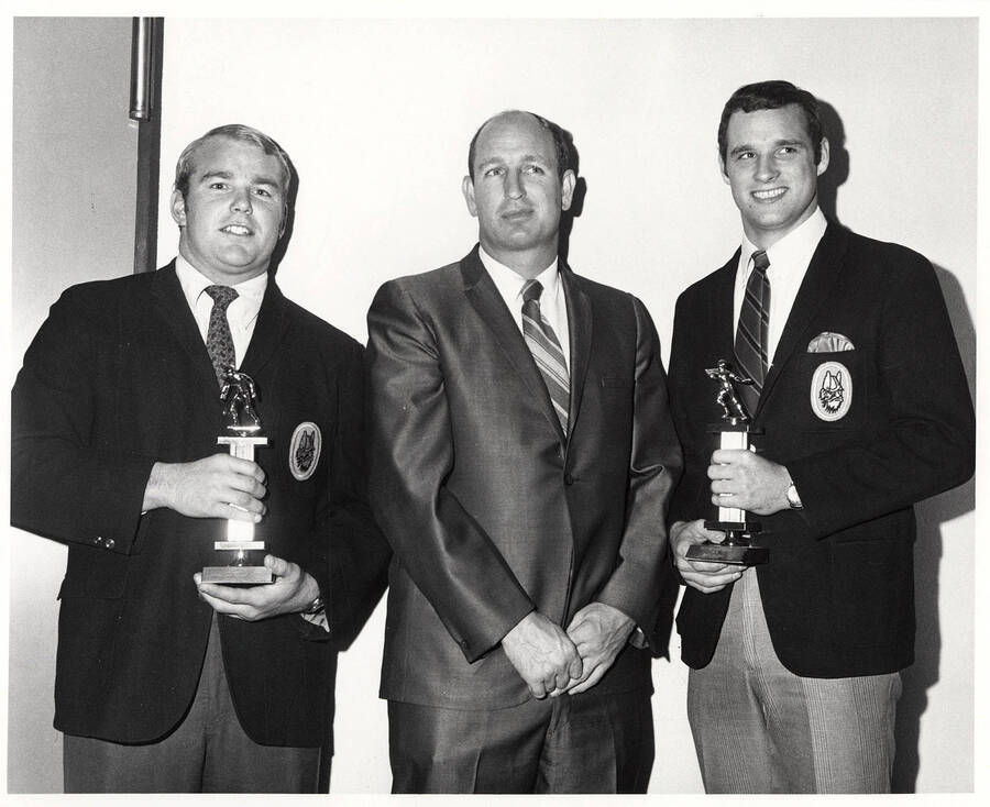Tom Nelson holding a trophy alongside coach Y.C. McNease, and Jerry Hendren holding the 'Most Valuable Player' trophy after the football awards for the University of Idaho.