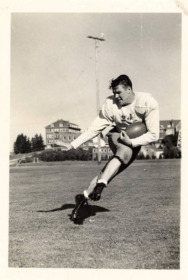 Earl Acuff, right halfback for the University of Idaho football team, running with a football for an action shot on the field.