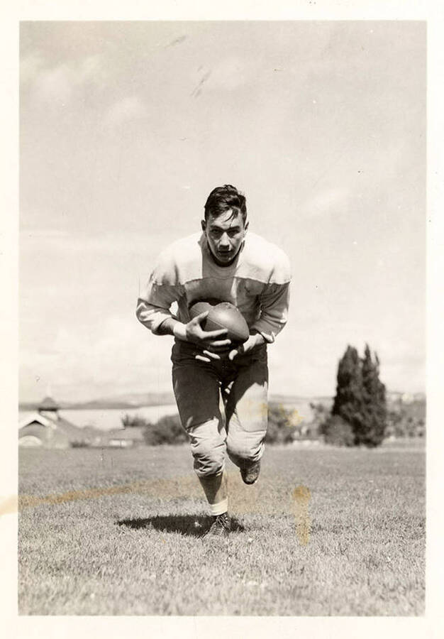 George Nixon, halfback for the University of Idaho football team, running towards the camera with a football.